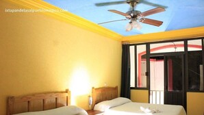 Habitación de hotel con dos camas, ventilador de techo y ventana con vista al exterior.