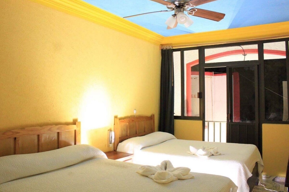 Habitación de hotel con dos camas, ventilador de techo y ventana con vista al exterior.