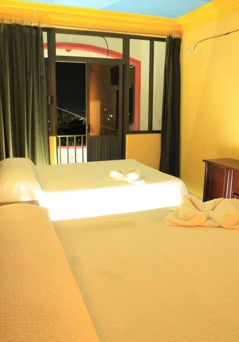 A hotel room with a bed, a small bedside table, and a view of the outside balcony.