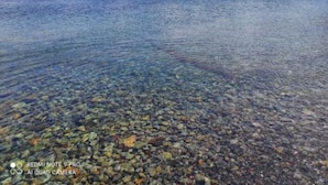 A clear view of a rocky shoreline with a sailboat in the distance.