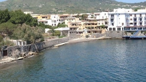 A coastal town with buildings along the waterfront, a stone wall, and a hill in the background.