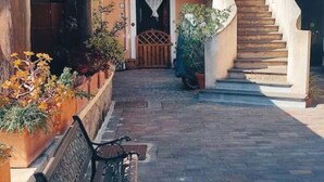 A narrow courtyard with a bench, potted plants, and a staircase leading to an upper level.