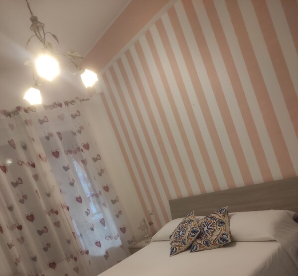 A bedroom with a bed, striped wall, and heart-patterned curtains.