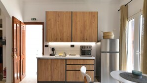 Cocina compacta con armarios de madera, refrigerador de acero inoxidable y una pequeña isla con una silla blanca.