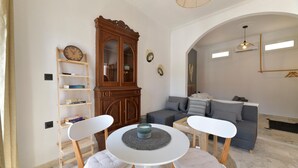 Una sala de estar con una mesa redonda, dos sillas blancas, un sofá gris y un aparador de madera.