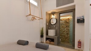 Un baño moderno con un espejo grande, un lavabo y una zona de ducha. Hay toallas en la cama y un extintor de incendios en la pared.