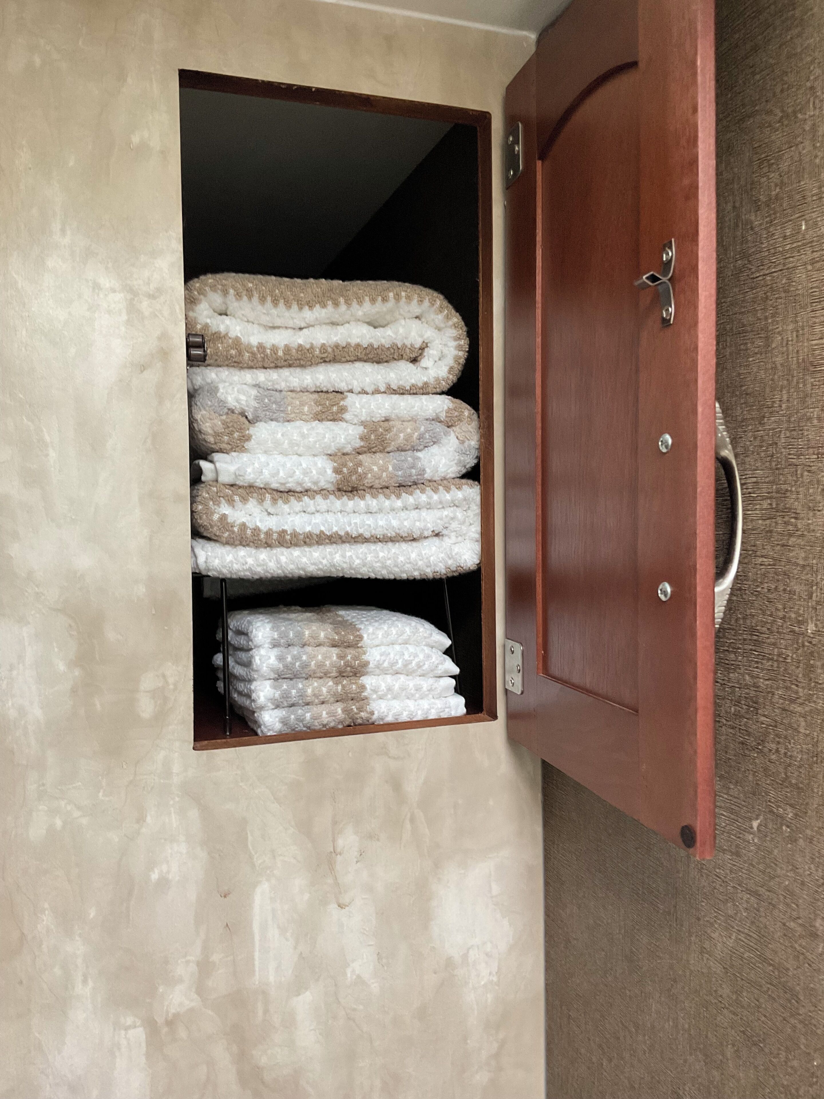 Une armoire en bois avec un miroir et une étagère où sont pliées des couvertures.