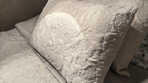 Una cama con edredón blanco texturizado y almohada decorativa con diseño en relieve.