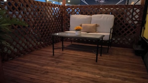 Una terraza de madera con un sofá blanco y una mesa, rodeada por un cerramiento de celosía.