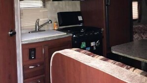 Een kleine keuken in een camper, met een magnetron, kookplaat en een klein spoelgedeelte.