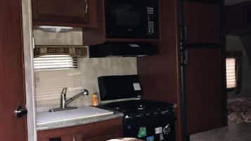 Een kleine keuken in een camper, met een magnetron, kookplaat en een klein spoelgedeelte.