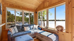 A wooden cabin with a large window overlooking a lake and dock. - Lakefront Home with Sandy Beach! Kayaks, SUP, Pedal boat, and more! (Shapleigh)