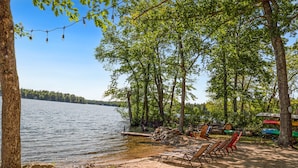 A lakeside campsite with a dock, chairs, and canoes. - Lakefront Home with Sandy Beach! Kayaks, SUP, Pedal boat, and more! (Shapleigh)