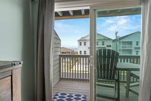 Enjoy the serene view from this balcony with a glass door, wooden deck, and a single Adirondack chair.