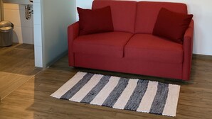 A red sofa with a striped rug, a bathroom with a sink and mirror, and a hanging light fixture. - Vacation apartments Gergert (Löwenstein)
