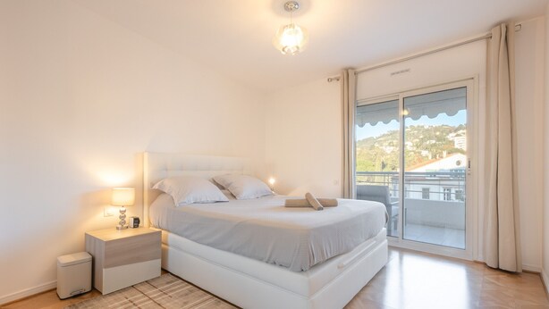 Quarto com cama, mesa de cabeceira e vista através de uma porta de correr.