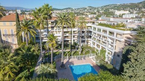 A multi-story hotel with a swimming pool surrounded by palm trees. - Le First (Cannes)