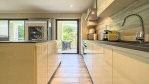 A modern kitchen with a central island, built-in appliances, and a view to an outdoor patio. - Le First (Cannes)