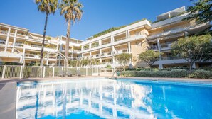 A hotel with a swimming pool, multiple balconies, and palm trees. - Le First (Cannes)