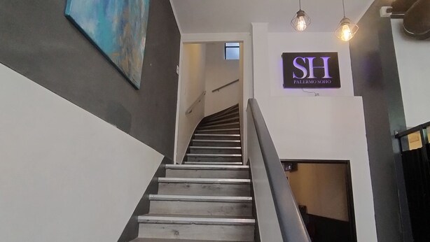 A staircase with a modern design, a sign for 'SH PALERMO SOHO', and a painting on the wall. - Sweet Home Palermo Soho Hostel (Buenos Aires)