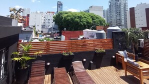 A rooftop terrace with wooden benches and planters, surrounded by city buildings. - Sweet Home Palermo Soho Hostel (Buenos Aires)