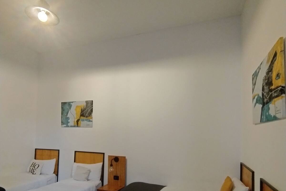A hotel room with two single beds, a nightstand, a wall-mounted lamp, and a painting.