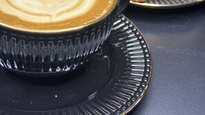 A cup of coffee with latte art on a black saucer, accompanied by a plate of croissants. - Sweet Home Palermo Soho Hostel (Buenos Aires)