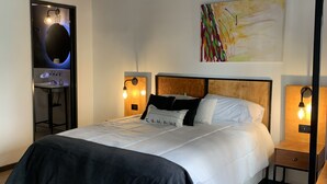 A neatly made bed with a black and white bedspread, two bedside tables with lamps, a wall-mounted abstract painting, and a mirror with a circular frame. - Sweet Home Palermo Soho Hostel (Buenos Aires)
