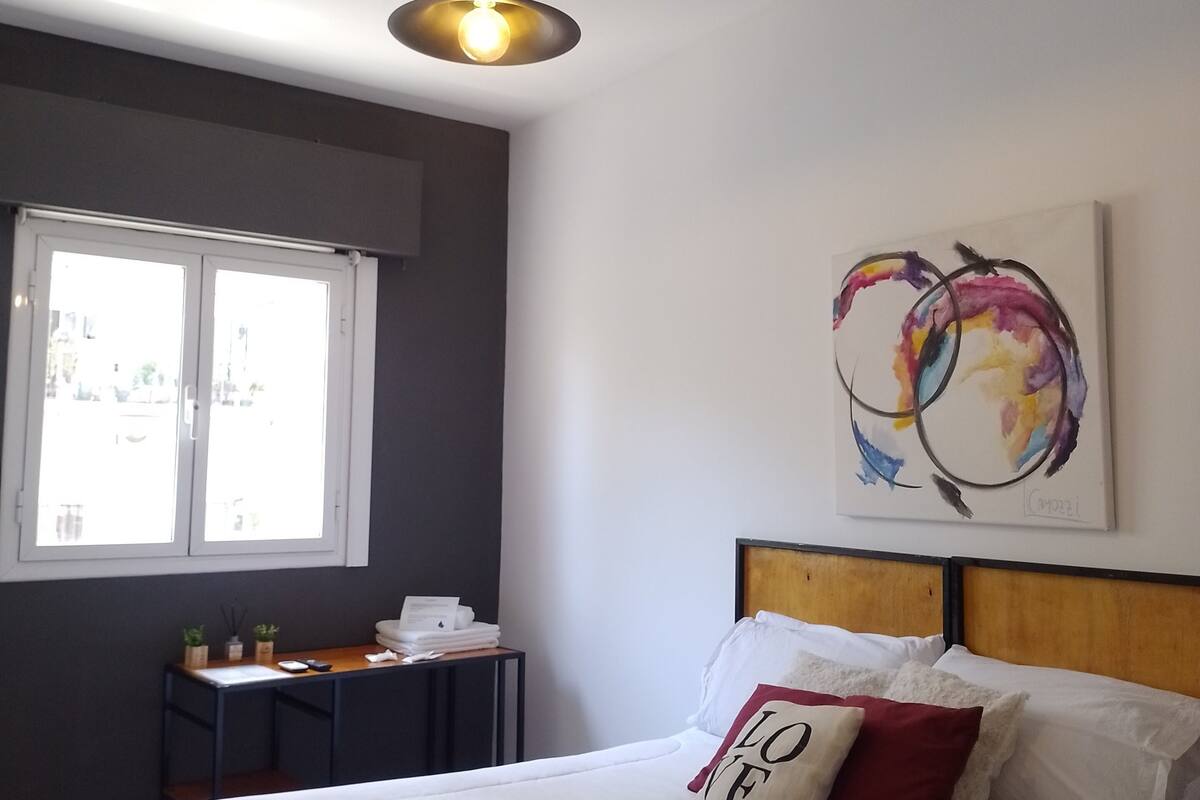 A bedroom with a bed, a bedside table, a window, and a ceiling light fixture.