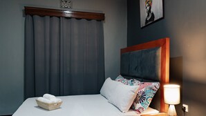 A neatly made bed with a basket of towels, a bedside lamp, and a painting on the wall. - Sleek, Beautiful  and Private Cottage (Arusha)