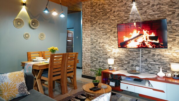 A living room with a stone wall, wooden ceiling, and a TV displaying a fireplace. - Sleek, Beautiful  and Private Cottage (Arusha)