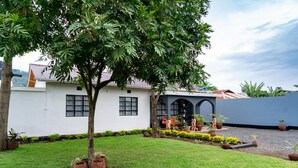 A white building with a tree in the front yard, potted plants, and a gravel path. - Sleek, Beautiful  and Private Cottage (Arusha)