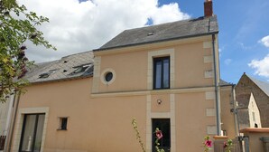 A two-story building with a beige facade, a tiled roof, and a small circular window on the second floor.