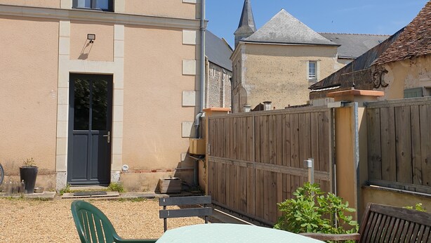 A courtyard with a table and chairs, a wooden fence, and a building with a door and windows.