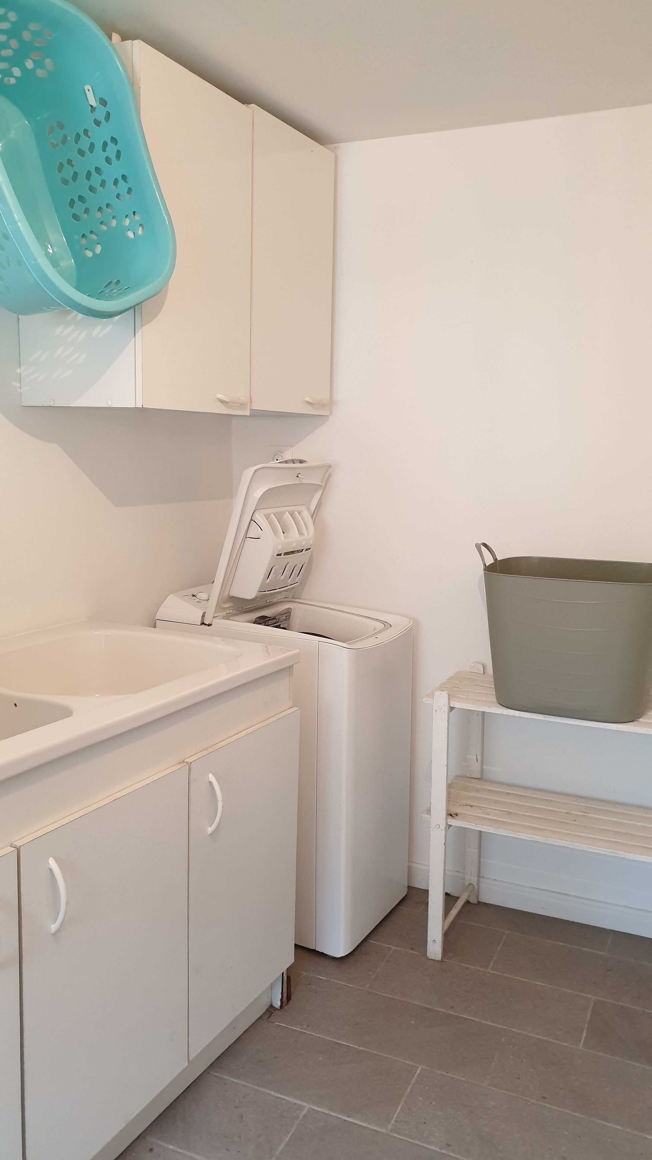 Un lavadero con lavadora, secadora, lavabo y un contenedor de almacenamiento grande.