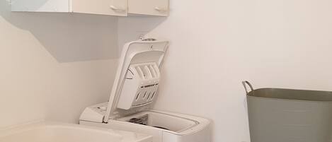Un lavadero con lavadora, secadora, lavabo y un contenedor de almacenamiento grande.