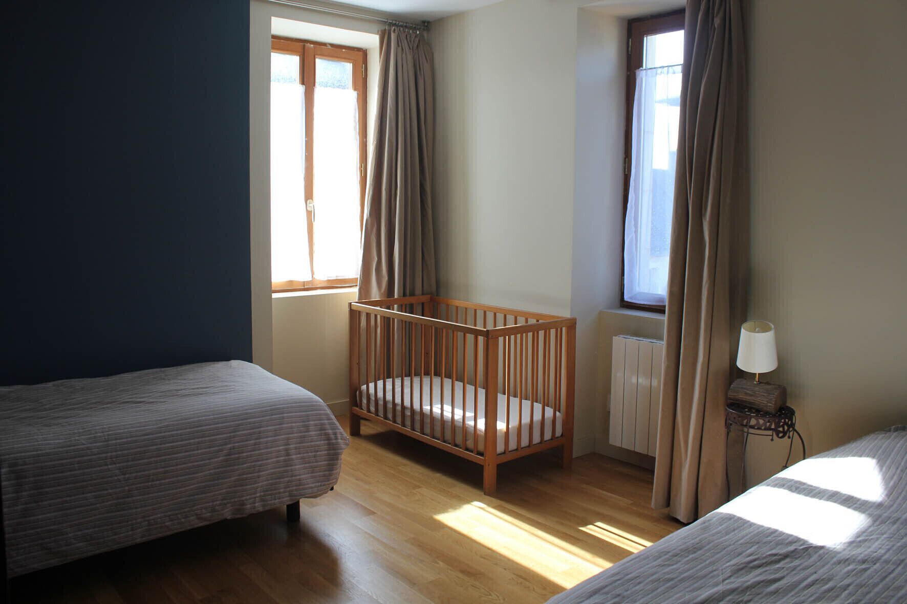 Une chambre avec deux lits, un berceau en bois, un radiateur et une lampe sur une table de chevet.
