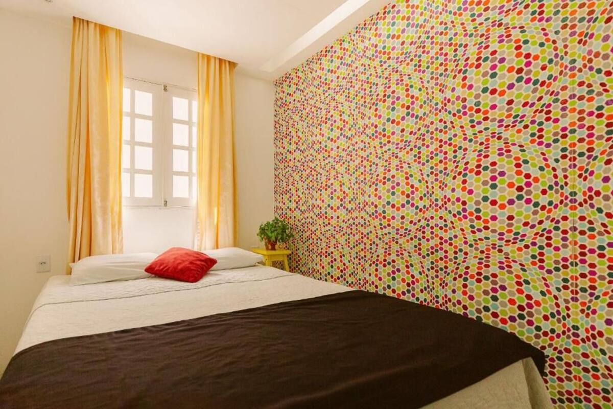 A bedroom with a bed, curtains, a window, and a colorful polka dot wall.