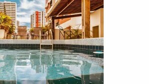 A swimming pool with a tiled deck, surrounded by lounge chairs and a building with multiple floors and balconies. - Vivaz Boutique Hotel (Recife)