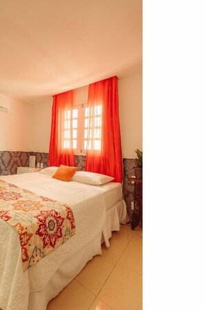 A bedroom with a large bed, red curtains, a patterned bedspread, and a small table with a plant. - Vivaz Boutique Hotel (Recife)