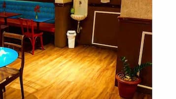 Um quarto com piso de madeira, uma mesa redonda com uma cadeira, um banco acolchoado azul, uma pia pequena e um vaso com planta.