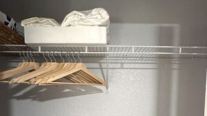 Een kast met een wit plank, houten kledinghangers en een zwarte stoel.