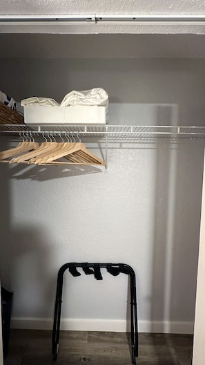 Un armario con un estante blanco, perchas de madera y una silla negra.