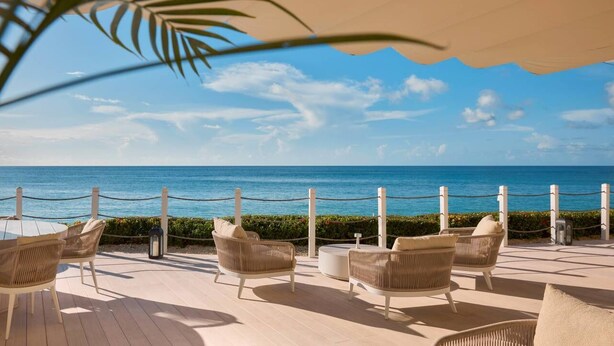 A deck with wicker chairs and a table overlooking the ocean. - Steps to Beach, Pool, Free Beach Club Access, Ocean/Sunset Views & Spacious! (Lower Carlton)