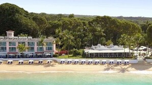 A beachfront hotel with a poolside area, palm trees, and a building with multiple windows and balconies. - Steps to Beach, Pool, Free Beach Club Access, Ocean/Sunset Views & Spacious! (Lower Carlton)
