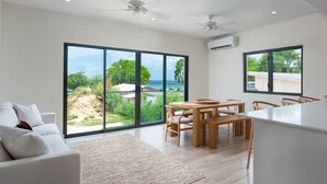 A modern living room with a large sliding glass door leading to a balcony with a view of the ocean. - Steps to Beach, Pool, Free Beach Club Access, Ocean/Sunset Views & Spacious! (Lower Carlton)