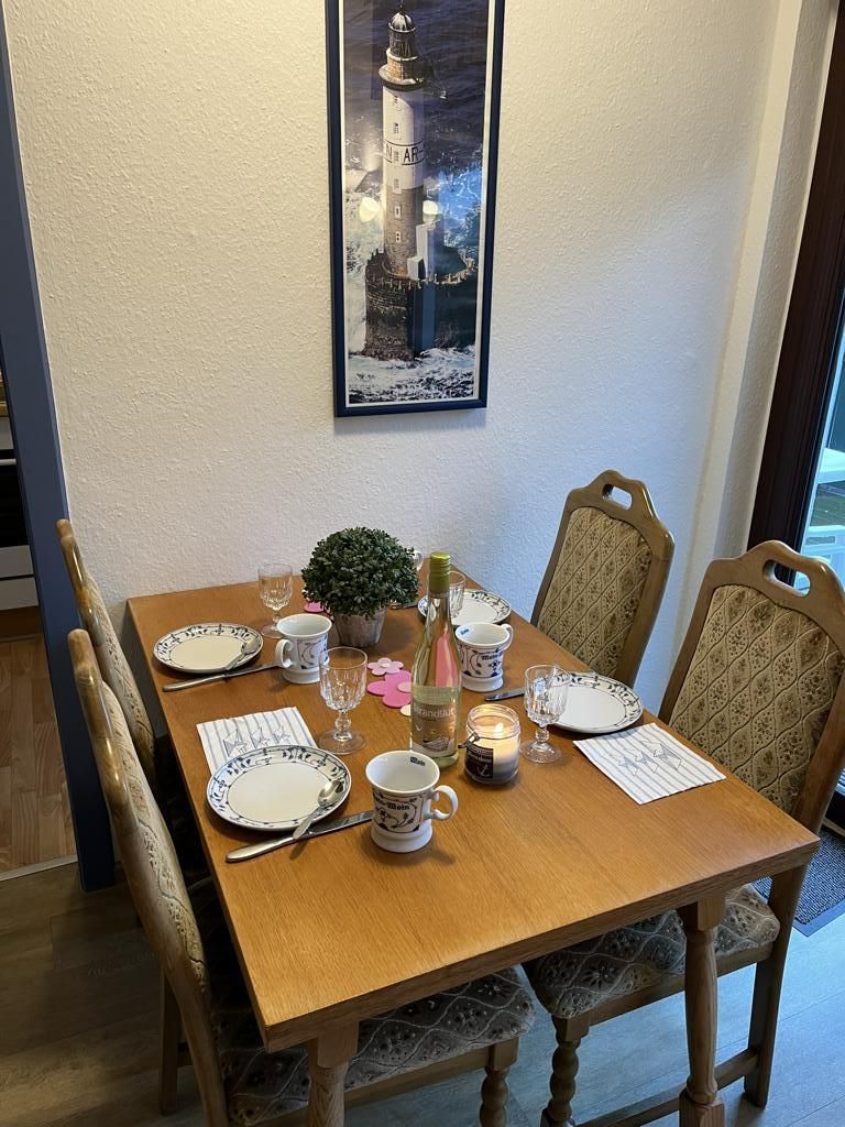 Ein Esstisch mit Geschirr, Tassen und einer Kerze, umgeben von gepolsterten Stühlen.