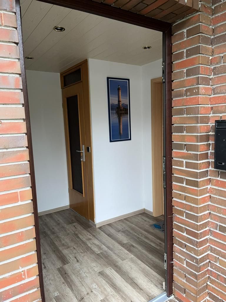 Ein Korridor mit Holzboden, einem gerahmten Bild an der Wand und einer Tür zu einem anderen Raum.