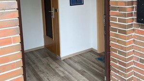 Un pasillo con suelo de madera, un cuadro en la pared y una puerta que da a otra habitación.