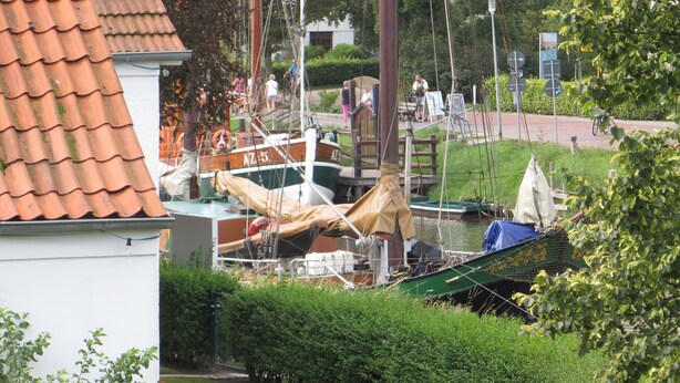 Un puerto deportivo con barcos amarrados, un edificio blanco de techo rojo y jardines bien cuidados.